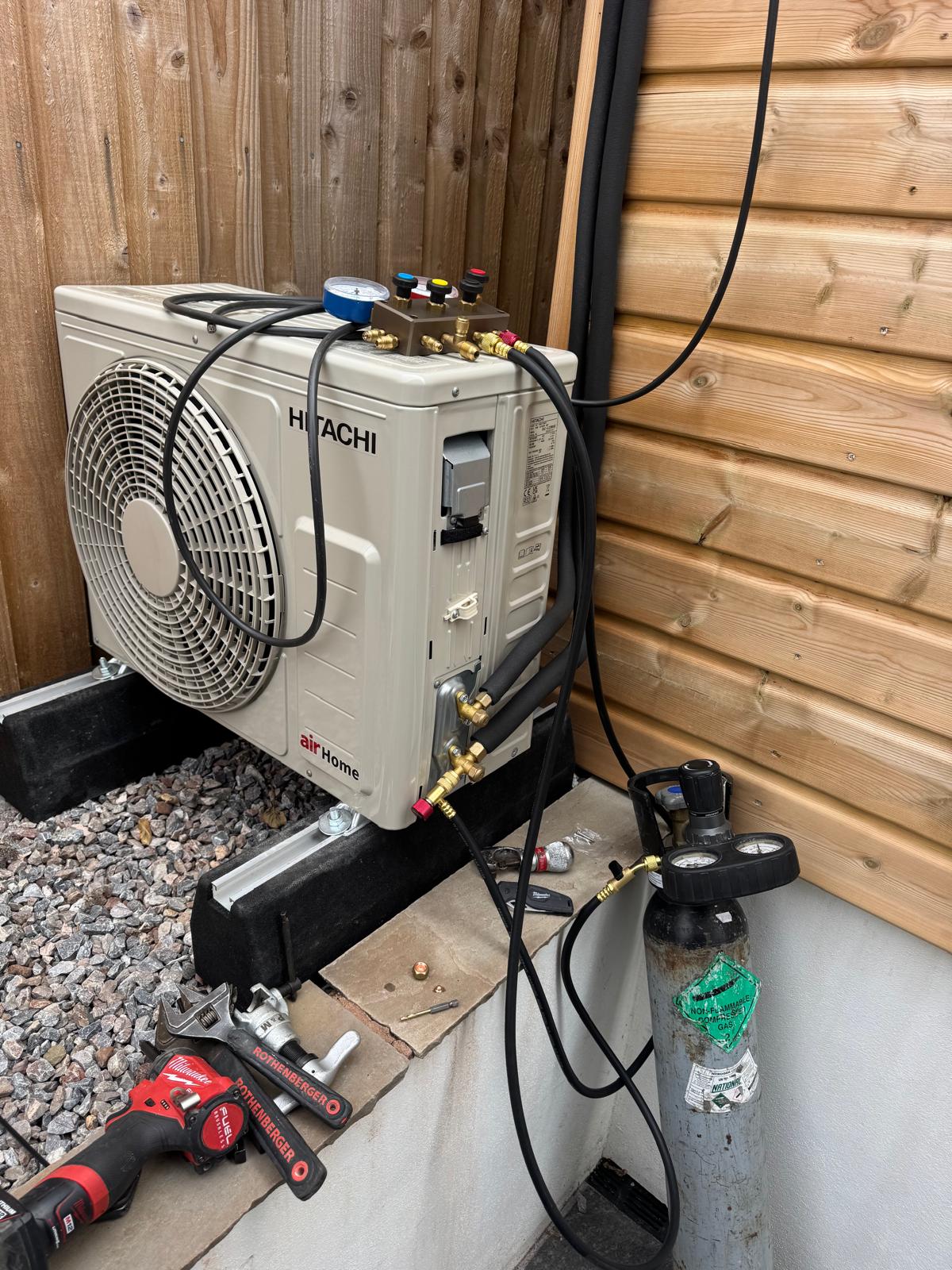 Polaris engineer commissioning a Hitachi air-source outdoor unit with gauges and tools